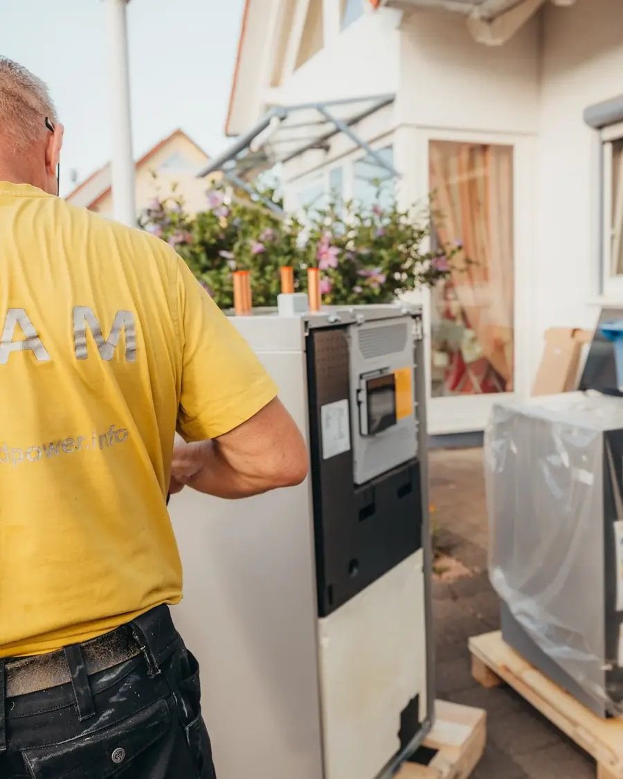 Monteur von Südpower stellt die Inneneinheit einer Wärmepumpe auf, daneben die verpackte Außeneinheit