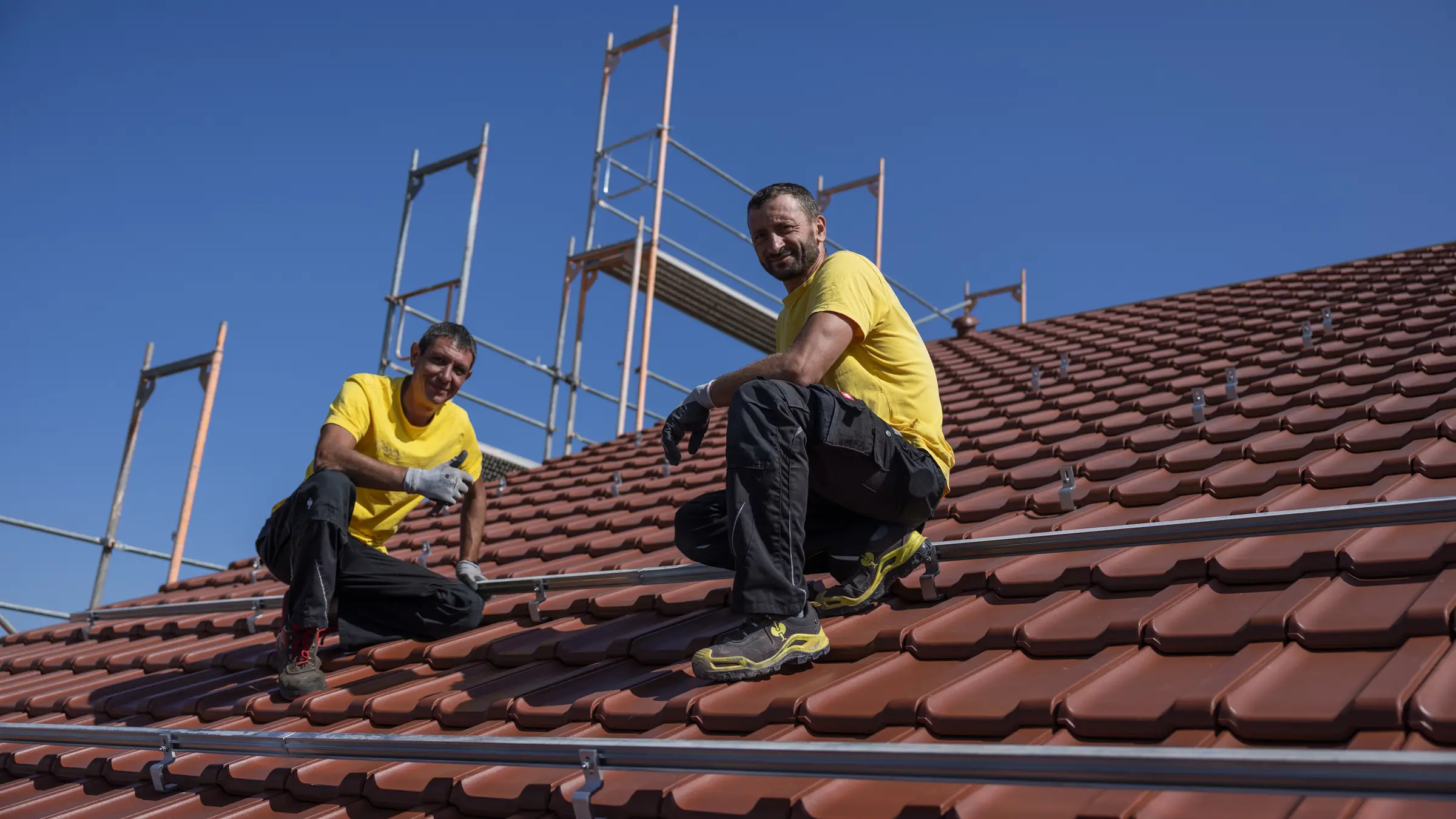 Zwei Monteure von Südpower auf einem Ziegeldach befestigen die Montageschienen für eine Photovoltaikanlage